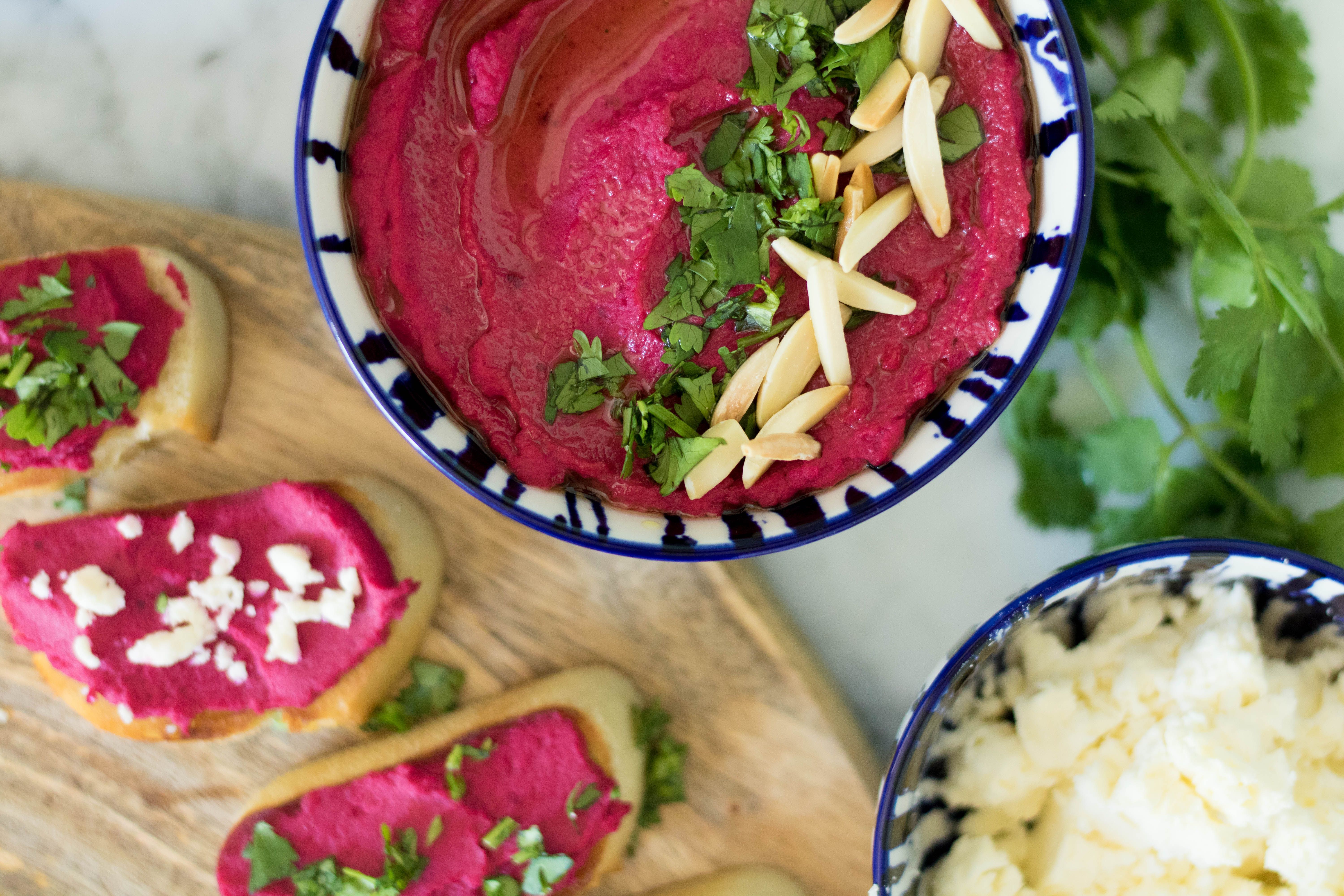 Fresh beetroot hummus with slivered almonds and parsley next to crostini toast appetizers
