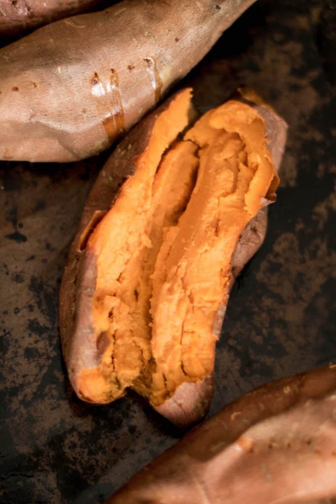 Oven baked sweet potato laying on black background