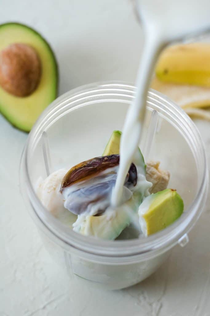 Adding the milk to the avocado, banana, and dates before blending