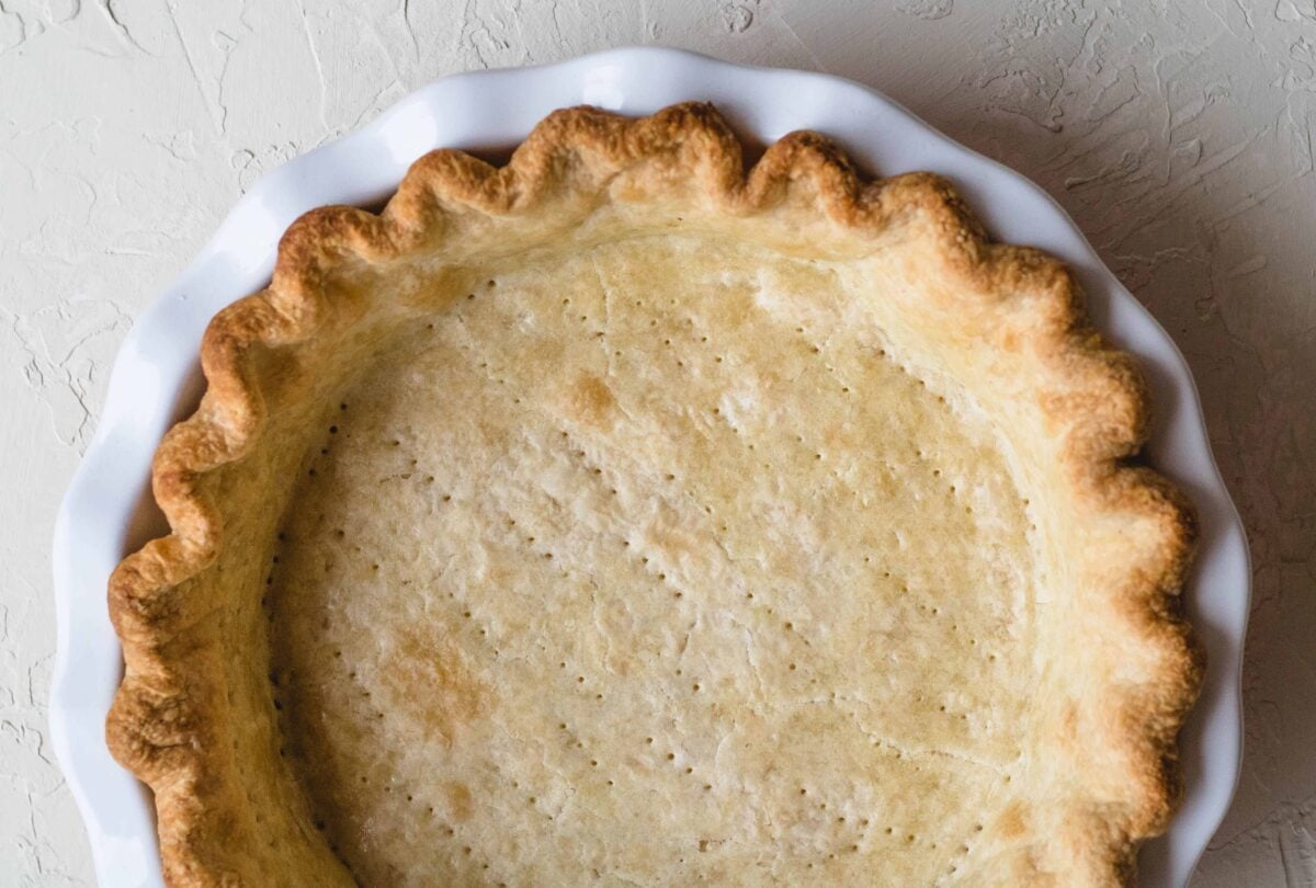 Fully blind-baked pie crust with golden fluted edges and docked bottom in a white pie dish.