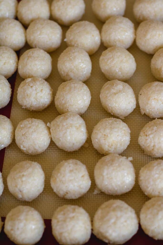 Uncoated coconut balls rolled by hand and lined up on a parchment lined tray.
