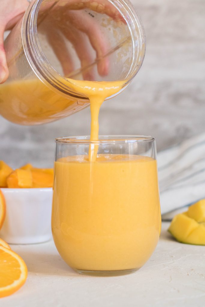 Pouring orange mango smoothie in a cup