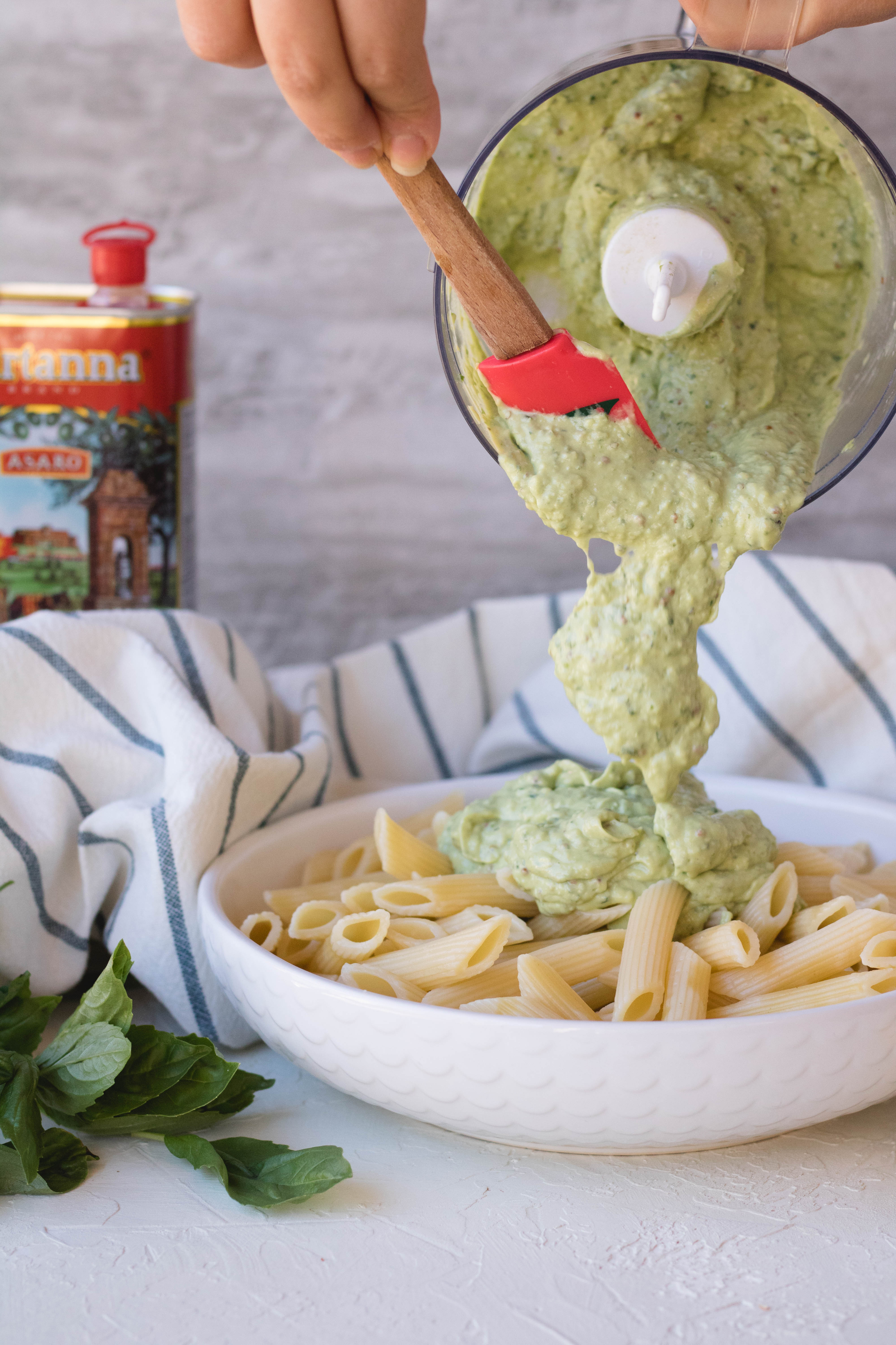 Pouring the avocado pasta sauce over the penne pasta