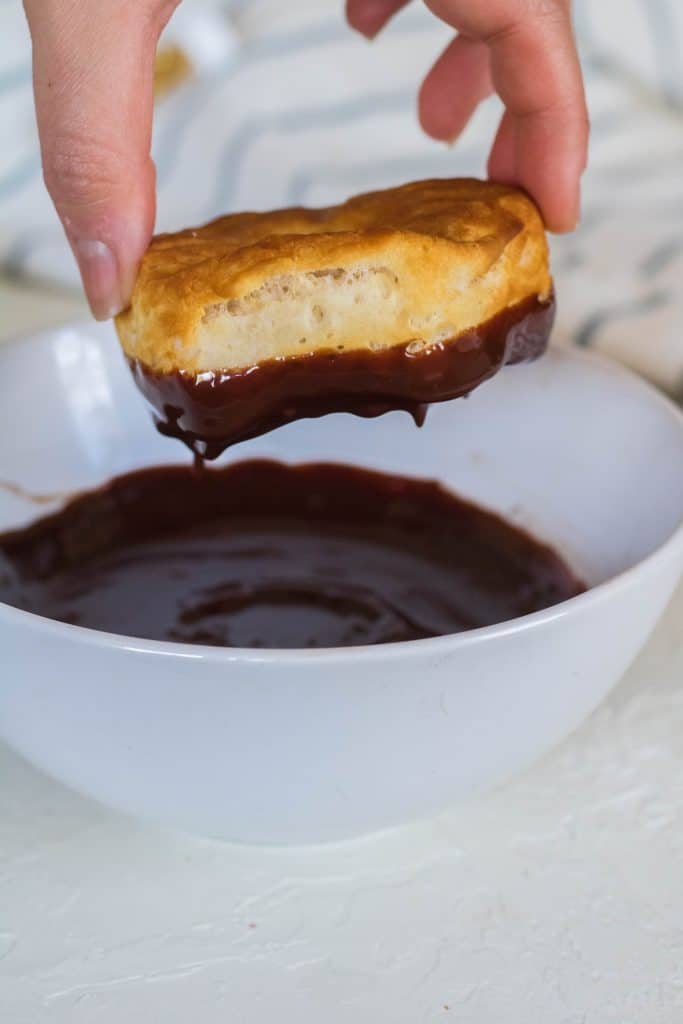 Dipping air fryer biscuit donut in chocolate ganache glaze