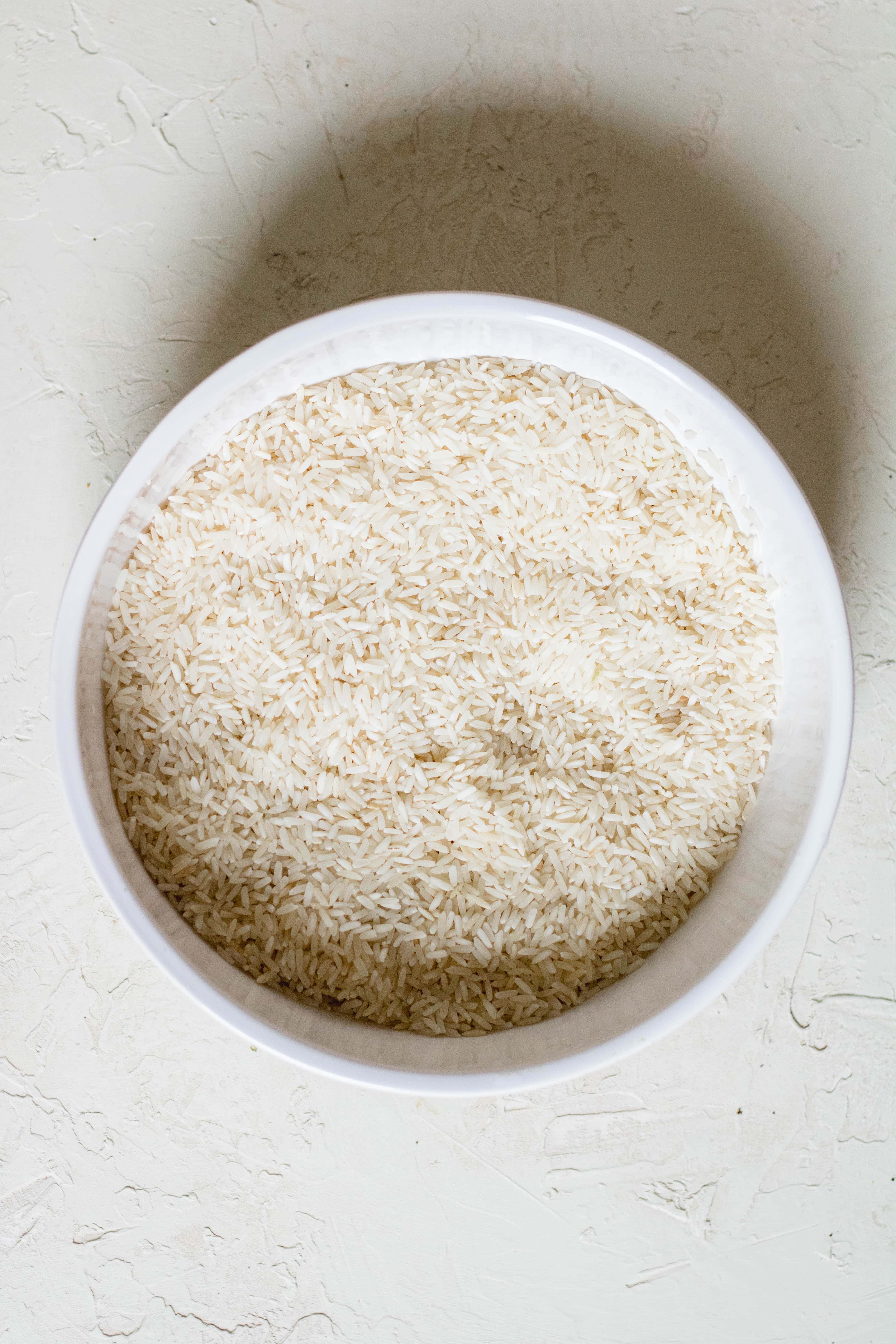 Uncooked long grain white rice in a white bowl before rinsing.