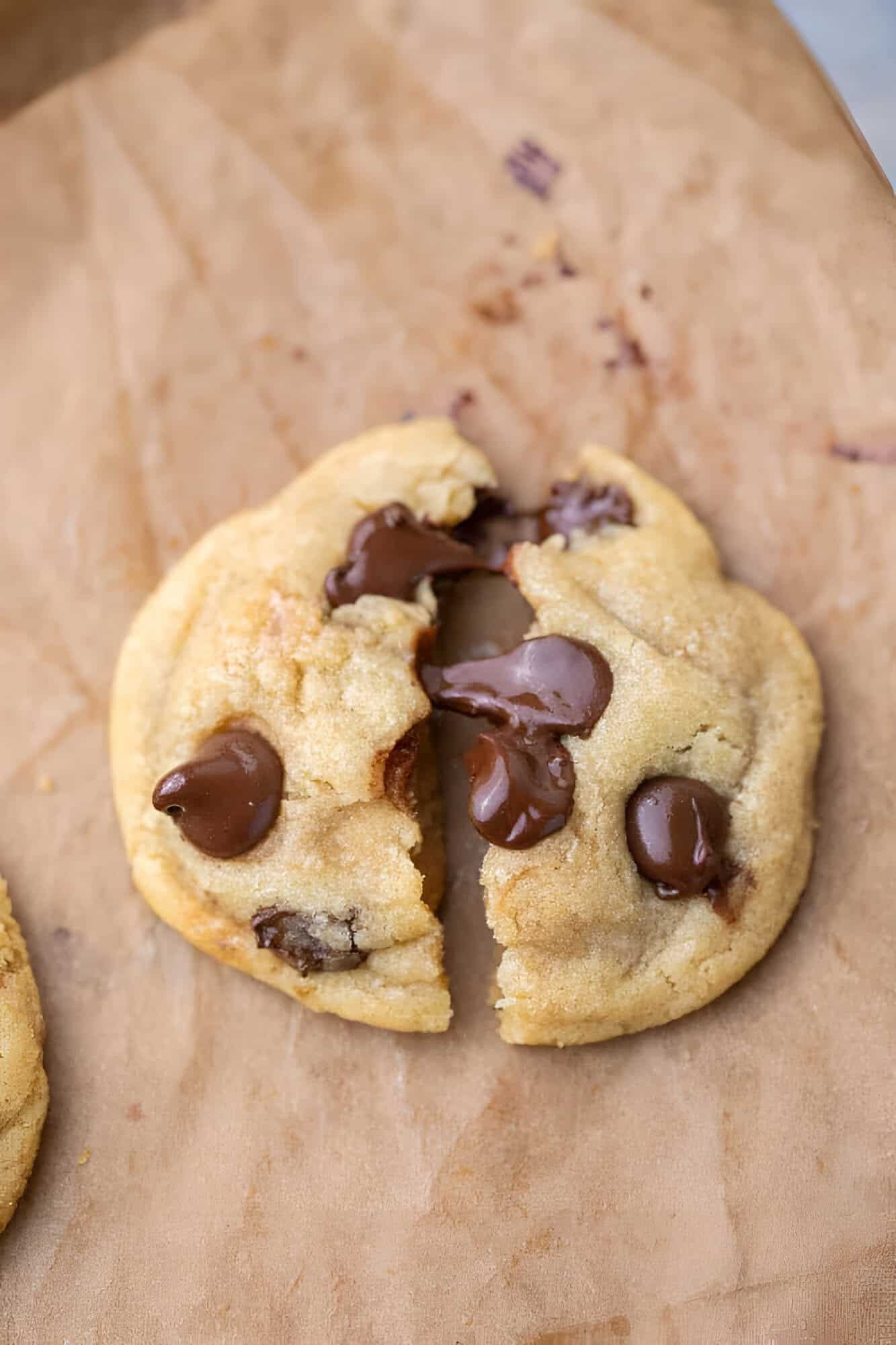 A small batch chocolate chip cookie broken in half with melted chocolate stretching between the pieces.