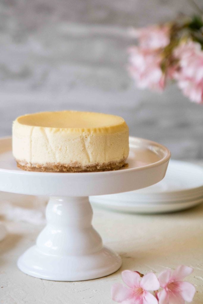 Whole 4-inch mini cheesecake on a cake stand with smooth top and graham cracker crust