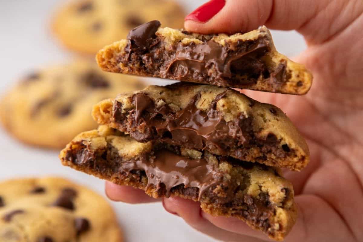 Hand holding a Nutella-stuffed chocolate chip cookie with melted hazelnut filling