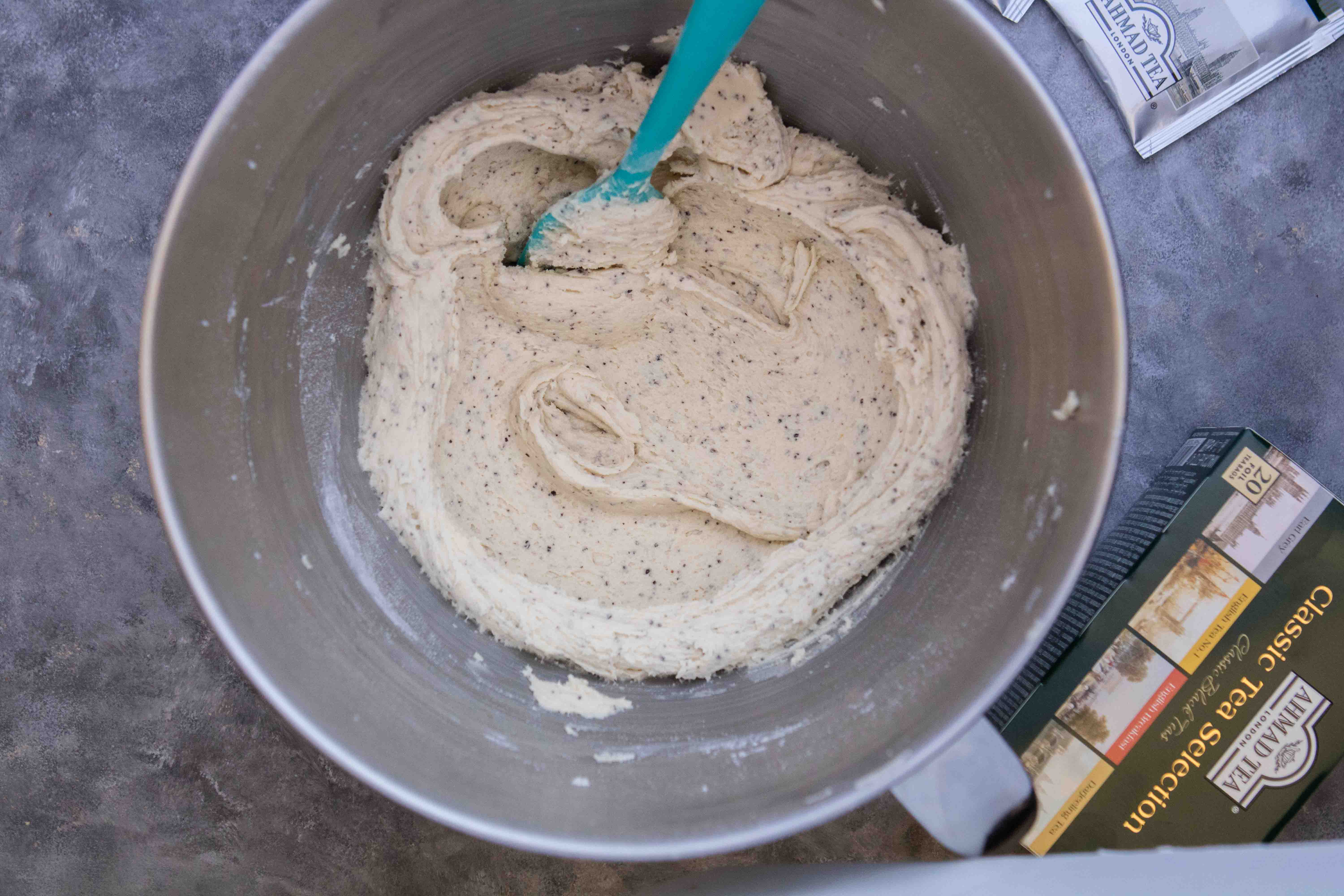 Butter, sugar and ground Earl Grey tea creamed together in a metal mixing bowl with a teal spatula.