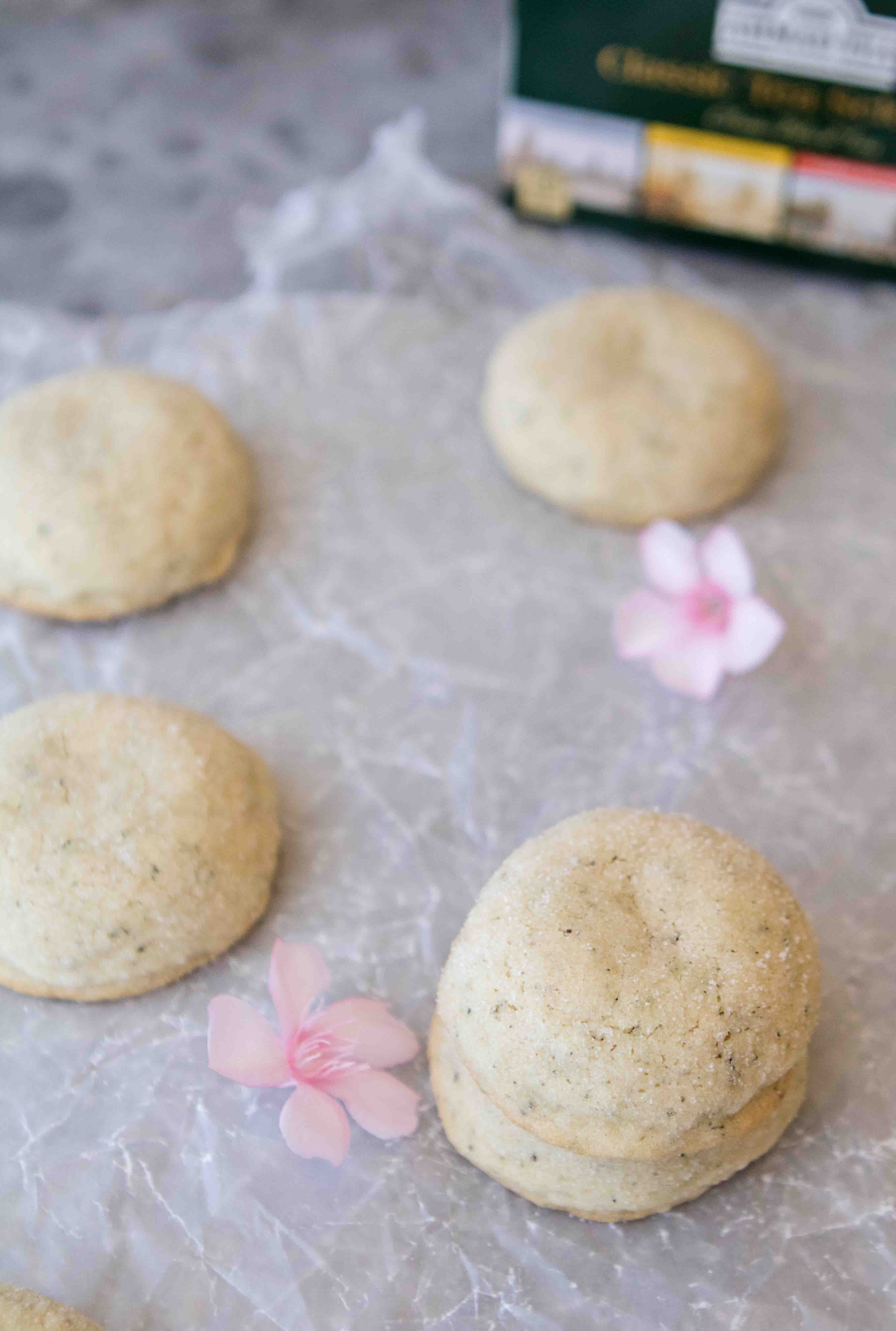 Thick baked Earl Grey cookies on parchment paper with pink flowers and a box of Earl Grey tea.