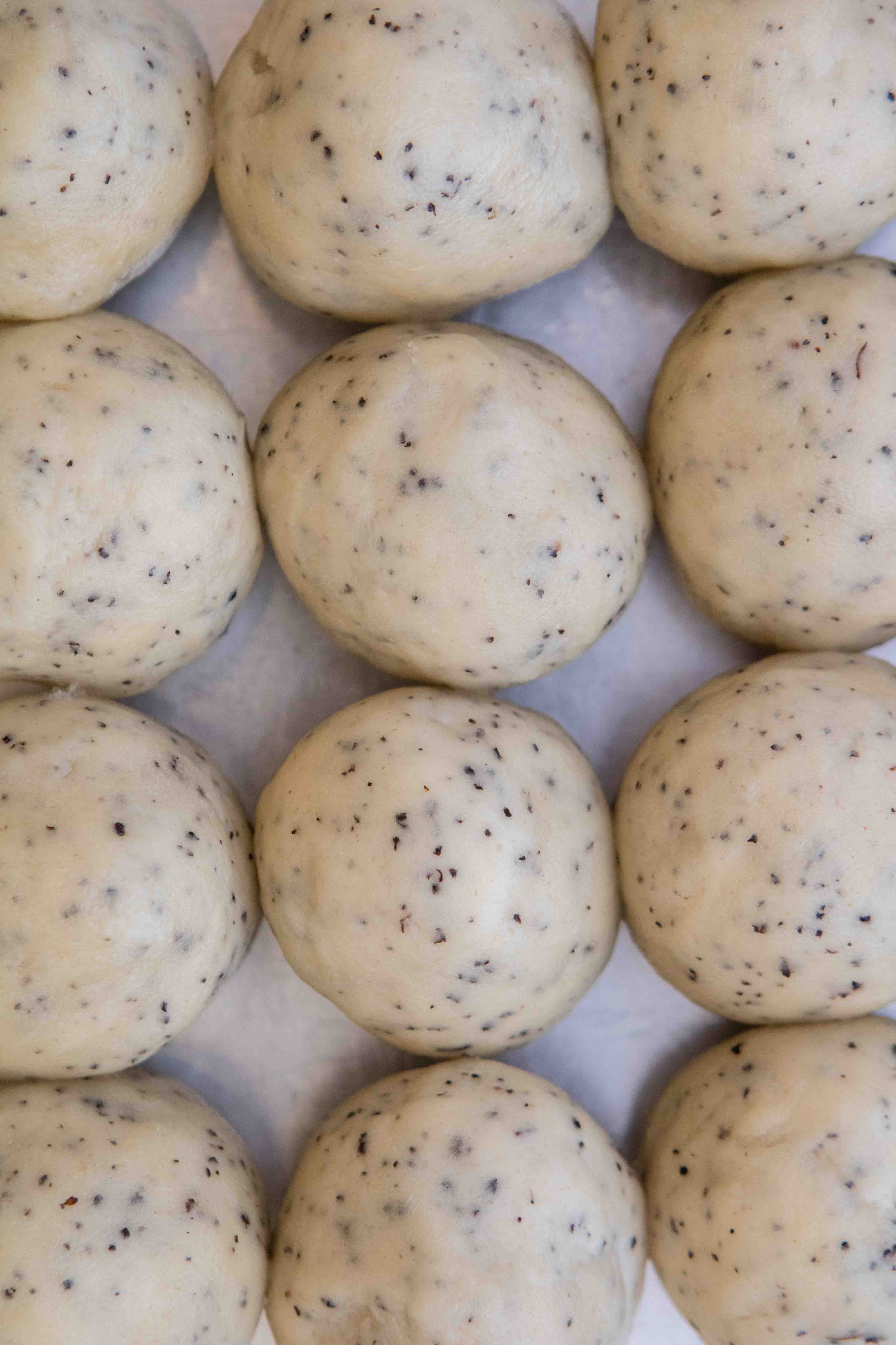 Rows of round Earl Grey cookie dough balls speckled with ground tea, lined up on a baking sheet.