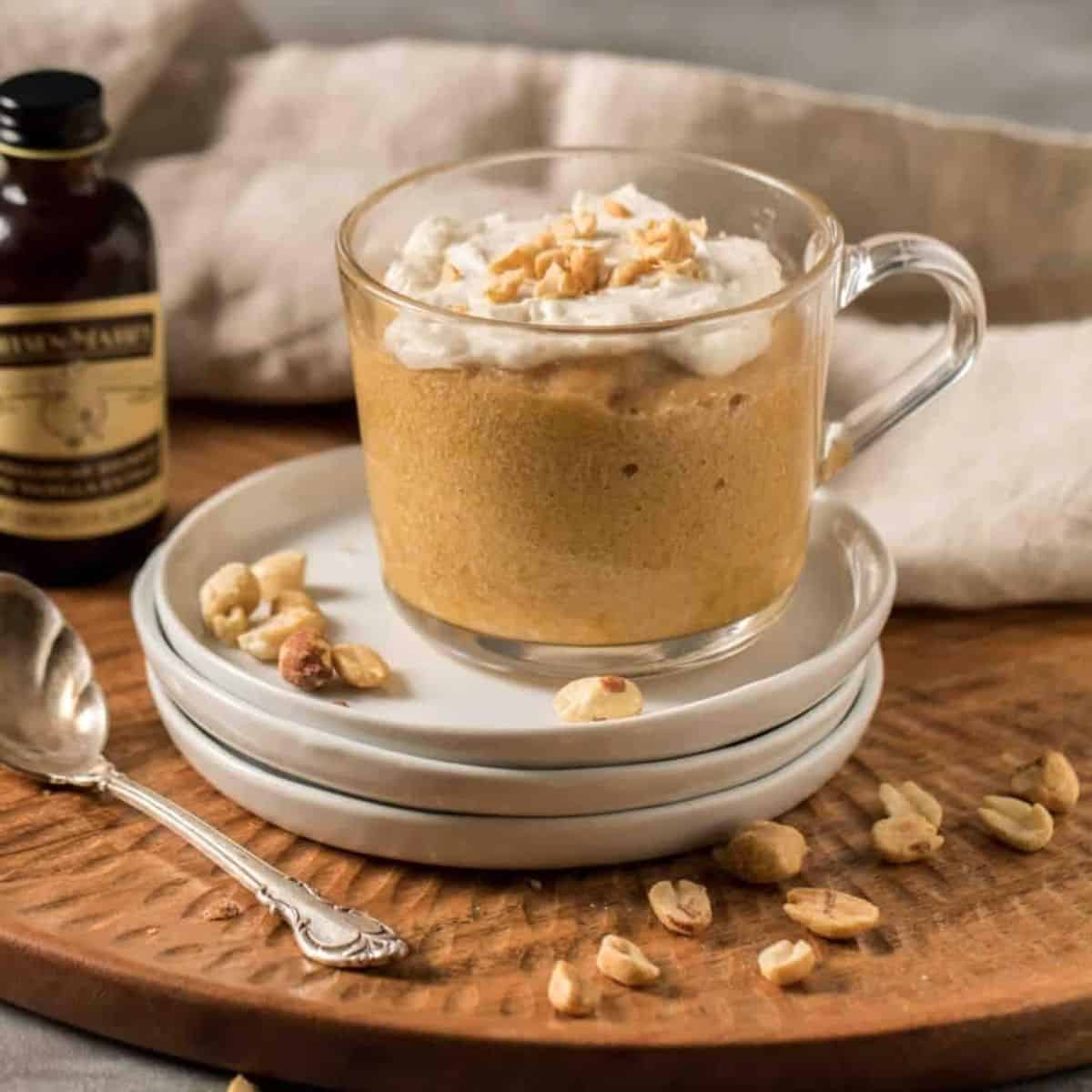 Moist peanut butter mug cake topped with whipped frosting and crushed peanuts in a glass mug.