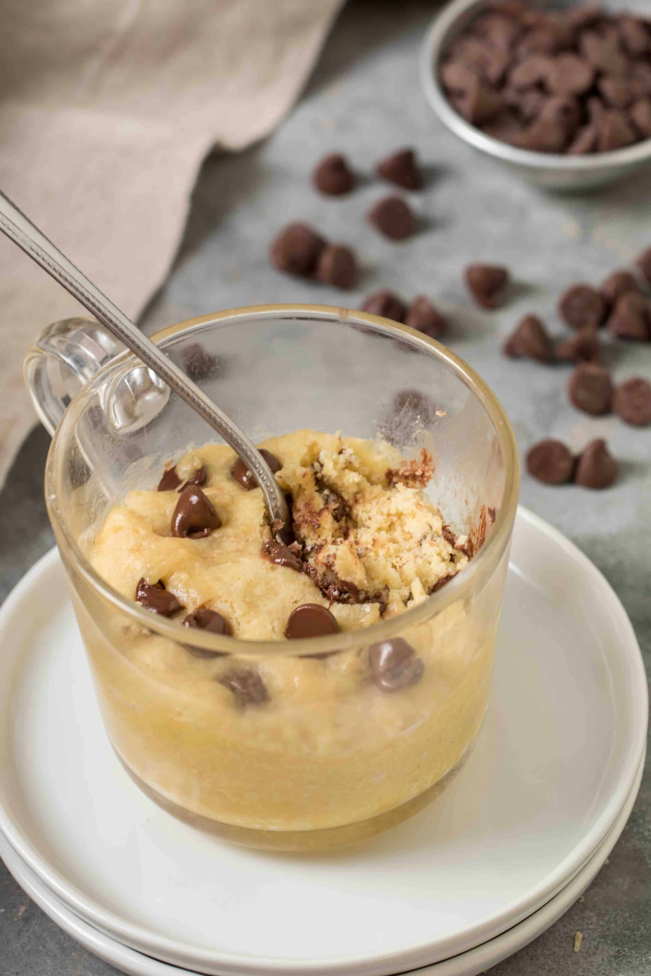 chocolate chip microwave cookie with a spoon in it and chocolate chips in the background