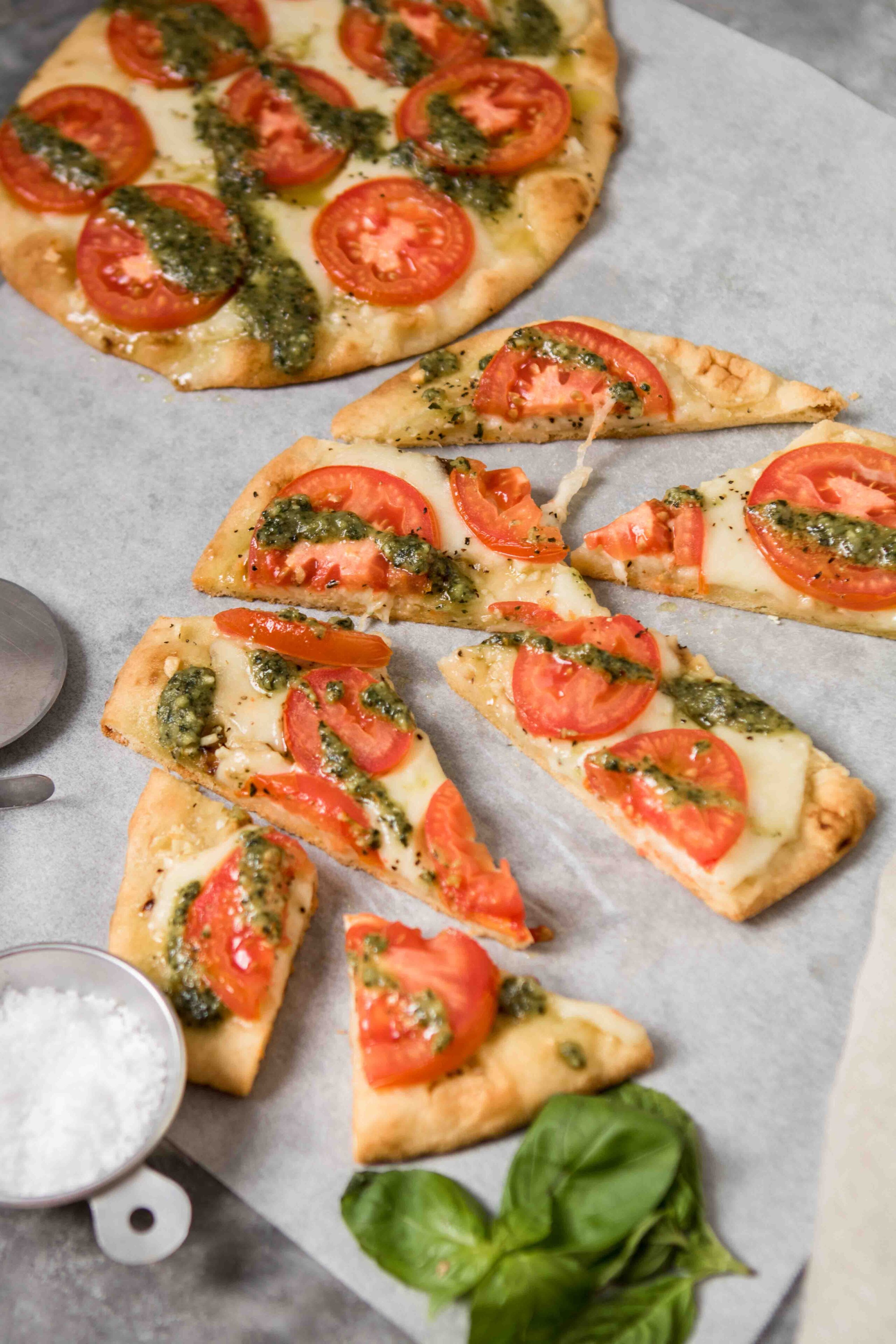 Sliced flat bread pizzas with sea salt and basil on the side