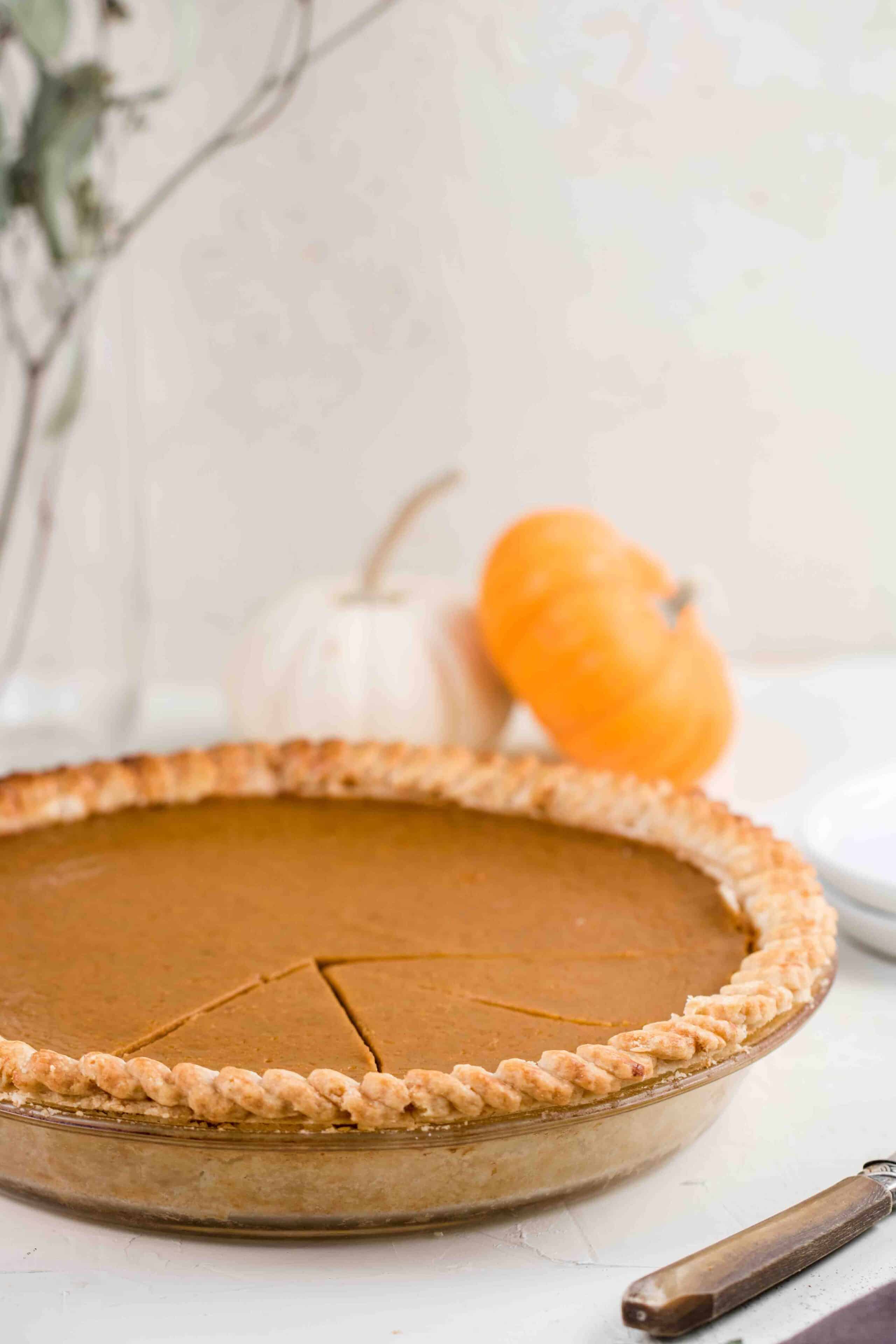 whole pumpkin pie with a few slices cut out and mini pumpkins in the background