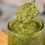 Homemade pesto in a little jar with a spoon scooping it out