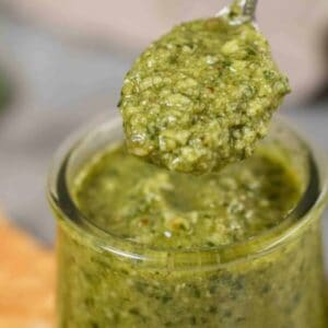Homemade pesto in a little jar with a spoon scooping it out