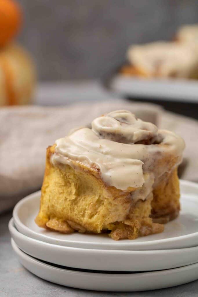 Pumpkin cinnamon roll with maple cream cheese frosting on stacked plates