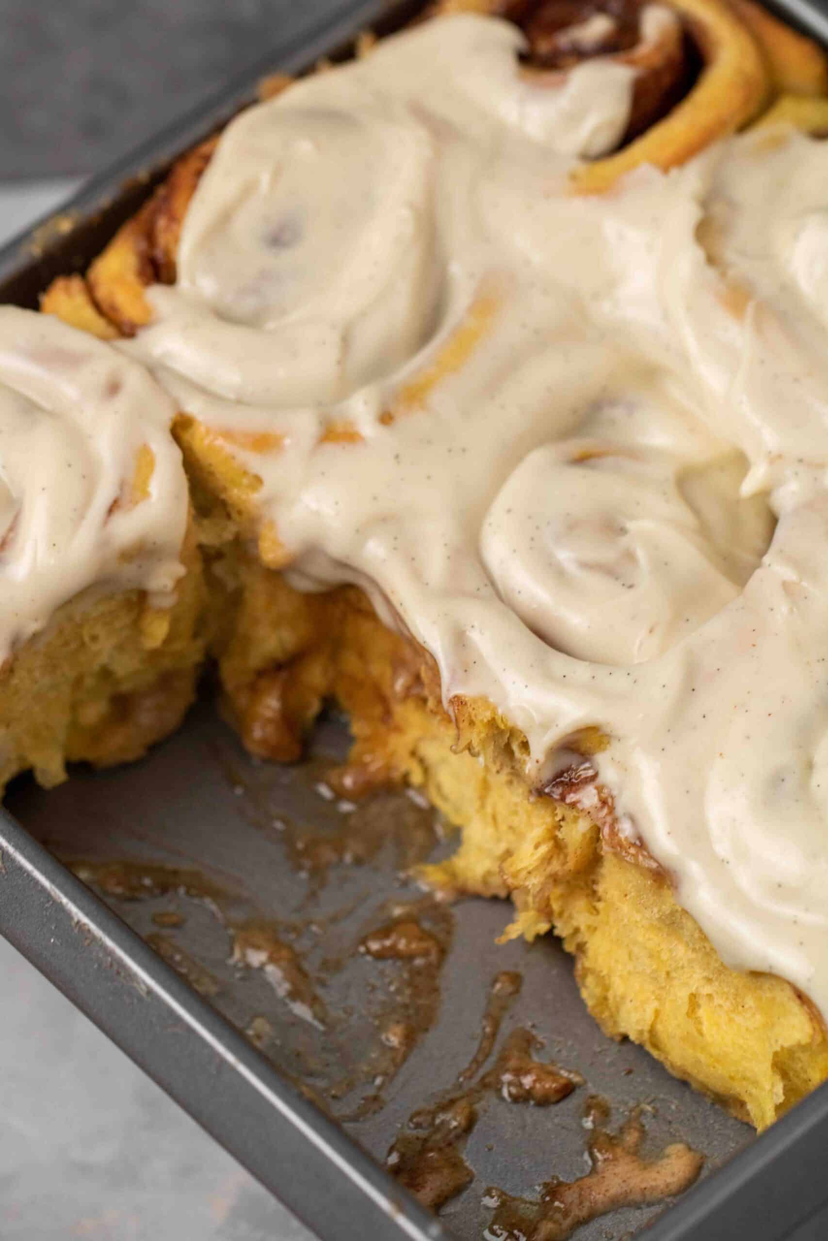 Pan of soft pumpkin cinnamon rolls covered in maple cream cheese frosting, ready to serve.