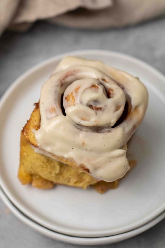 Finished pumpkin cinnamon roll on a plate with vanilla bean flecked maple frosting.