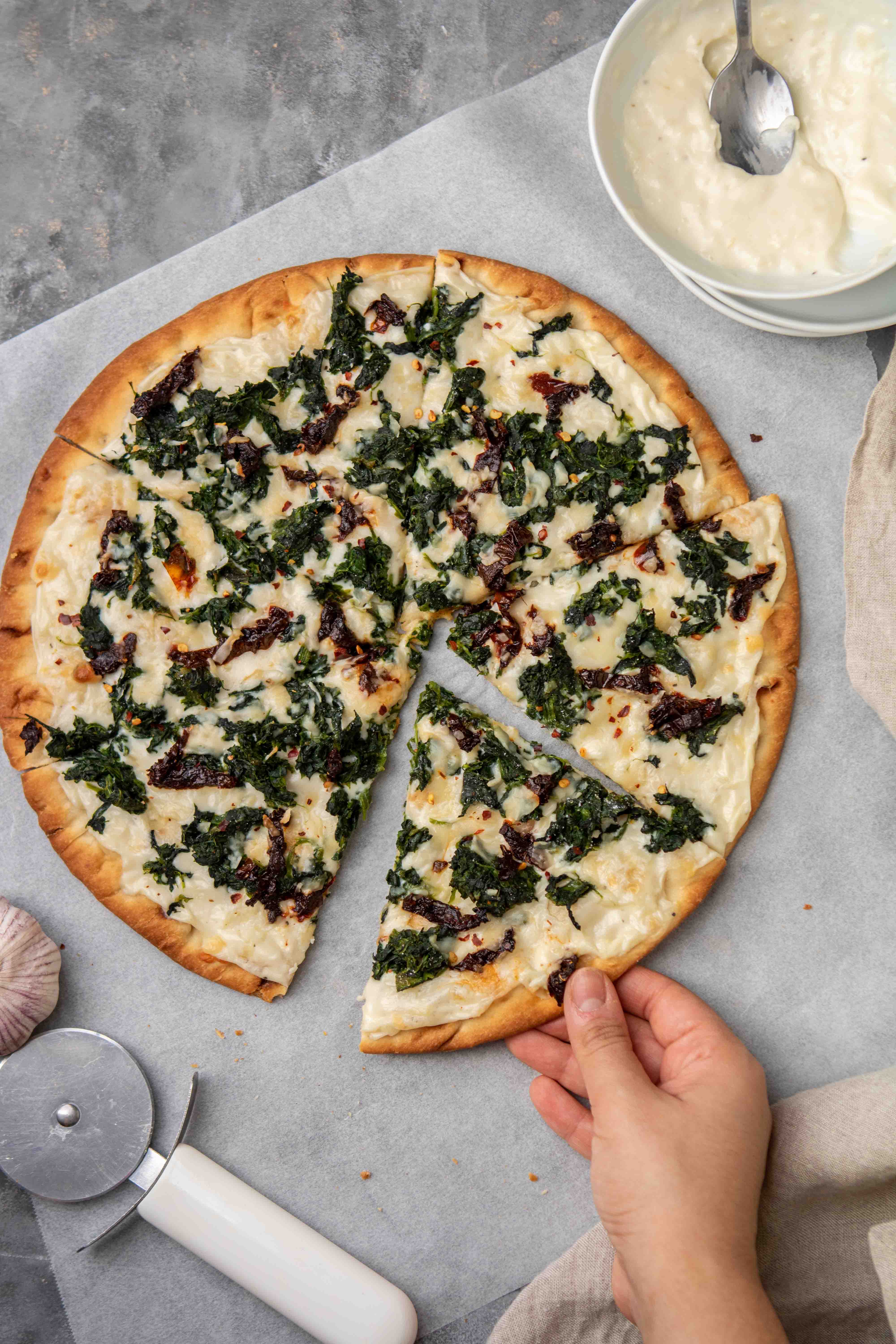 Hand grabbing pizza with white sauce slice