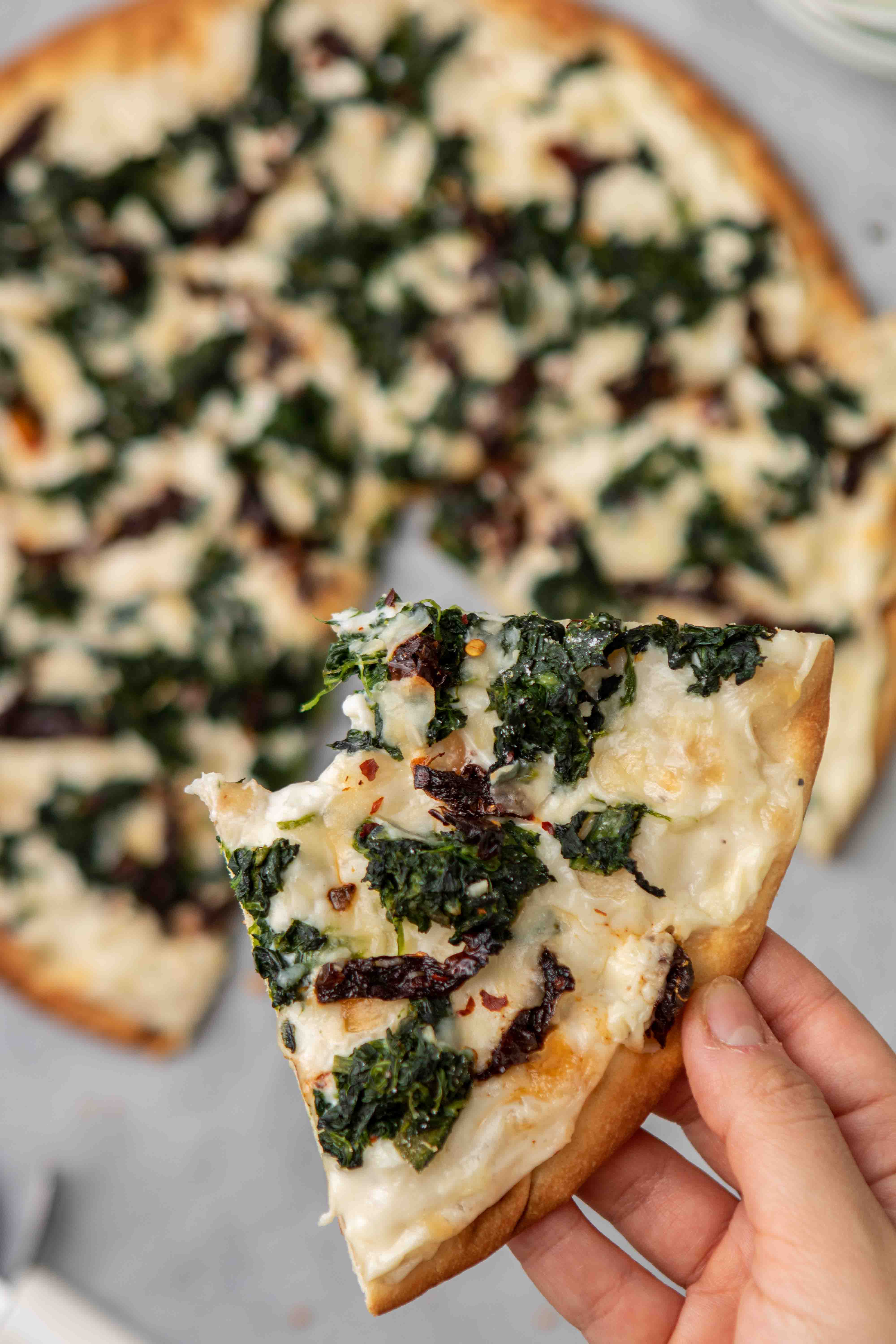 Close up of a spinach pizza with white sauce slice