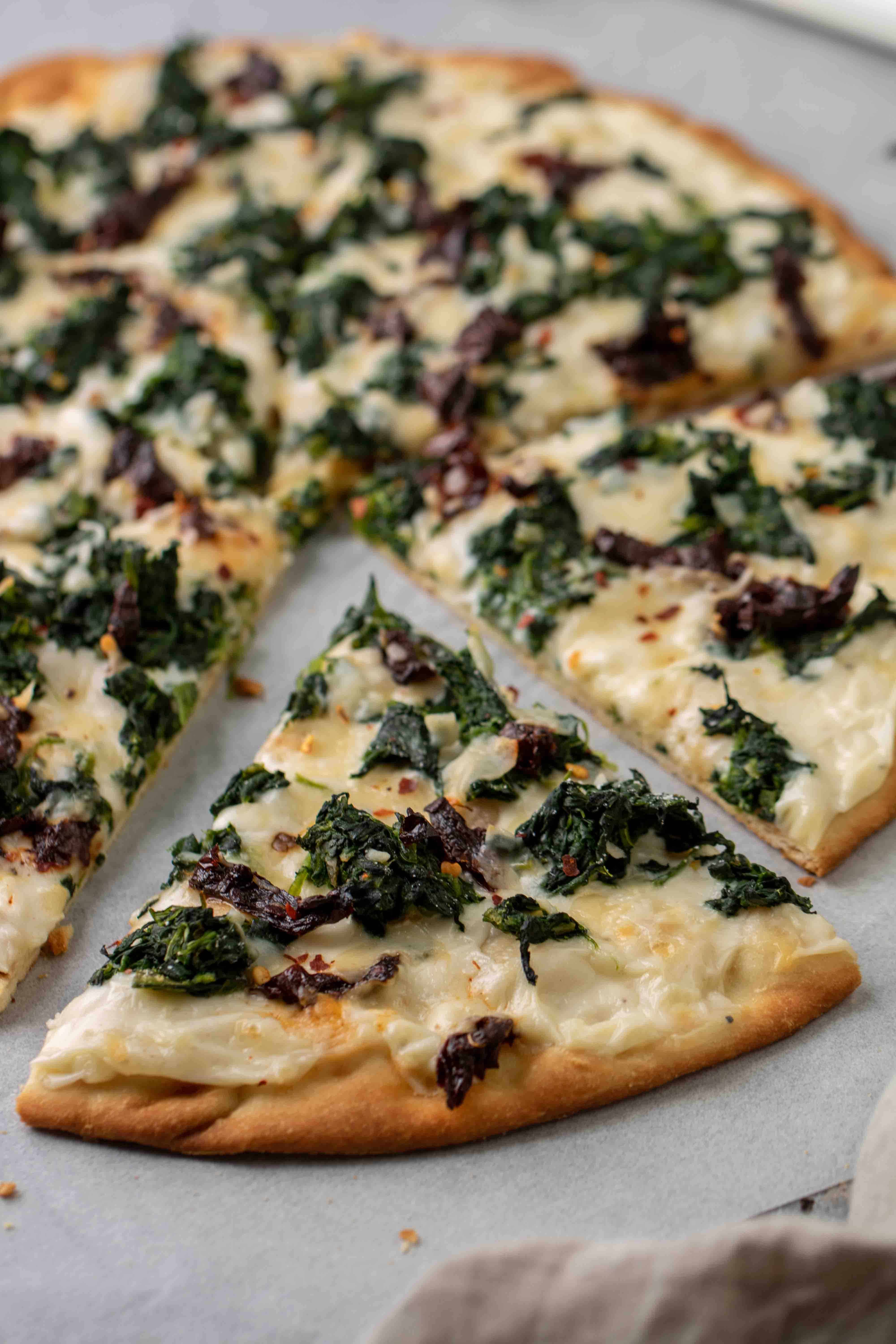 Pizza with white sauce, spinach and sun dried tomatoes