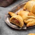 Cheese and ground beef crescent rolls on a metal tray with the front one cut in half to show the filling.