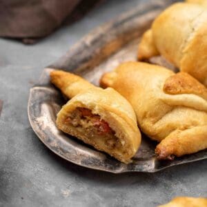 Cheese and ground beef crescent rolls on a metal tray with the front one cut in half to show the filling.