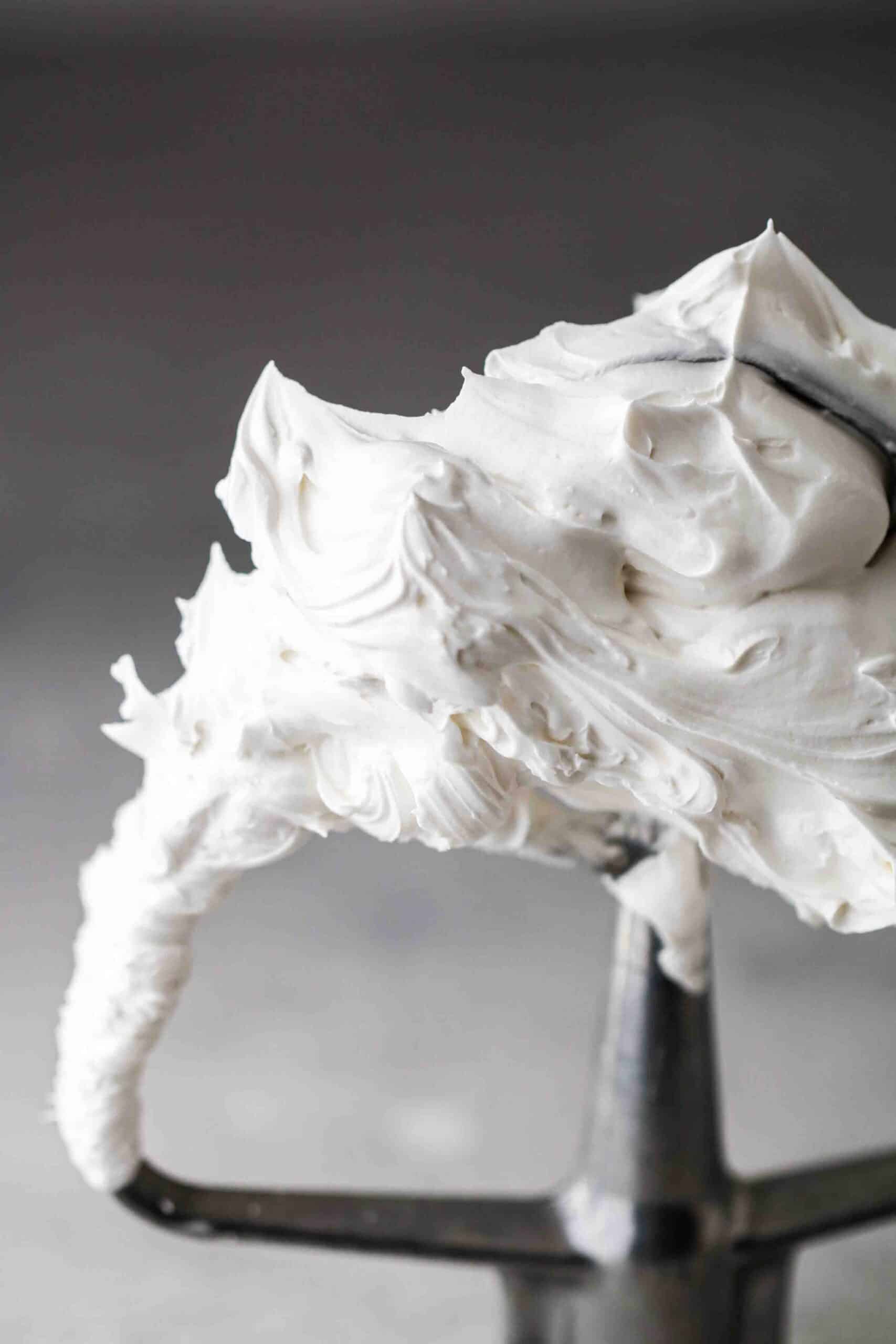 Stiff, glossy white meringue clinging to a stand mixer whisk attachment.