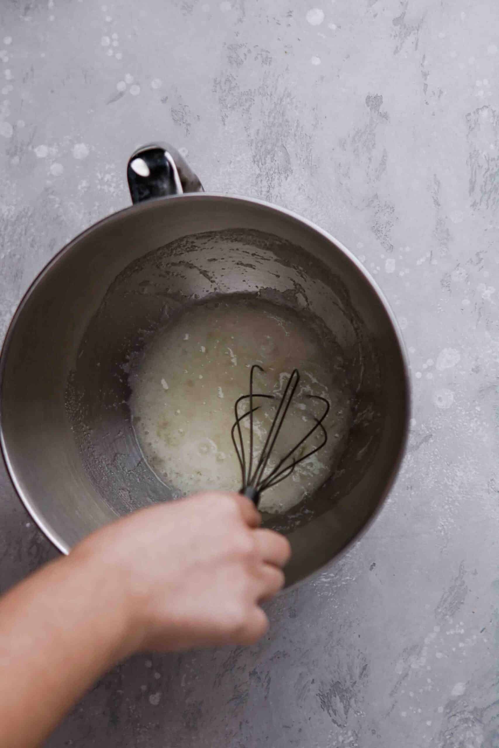 Egg whites and sugar being whisked by hand in a stand mixer bowl.