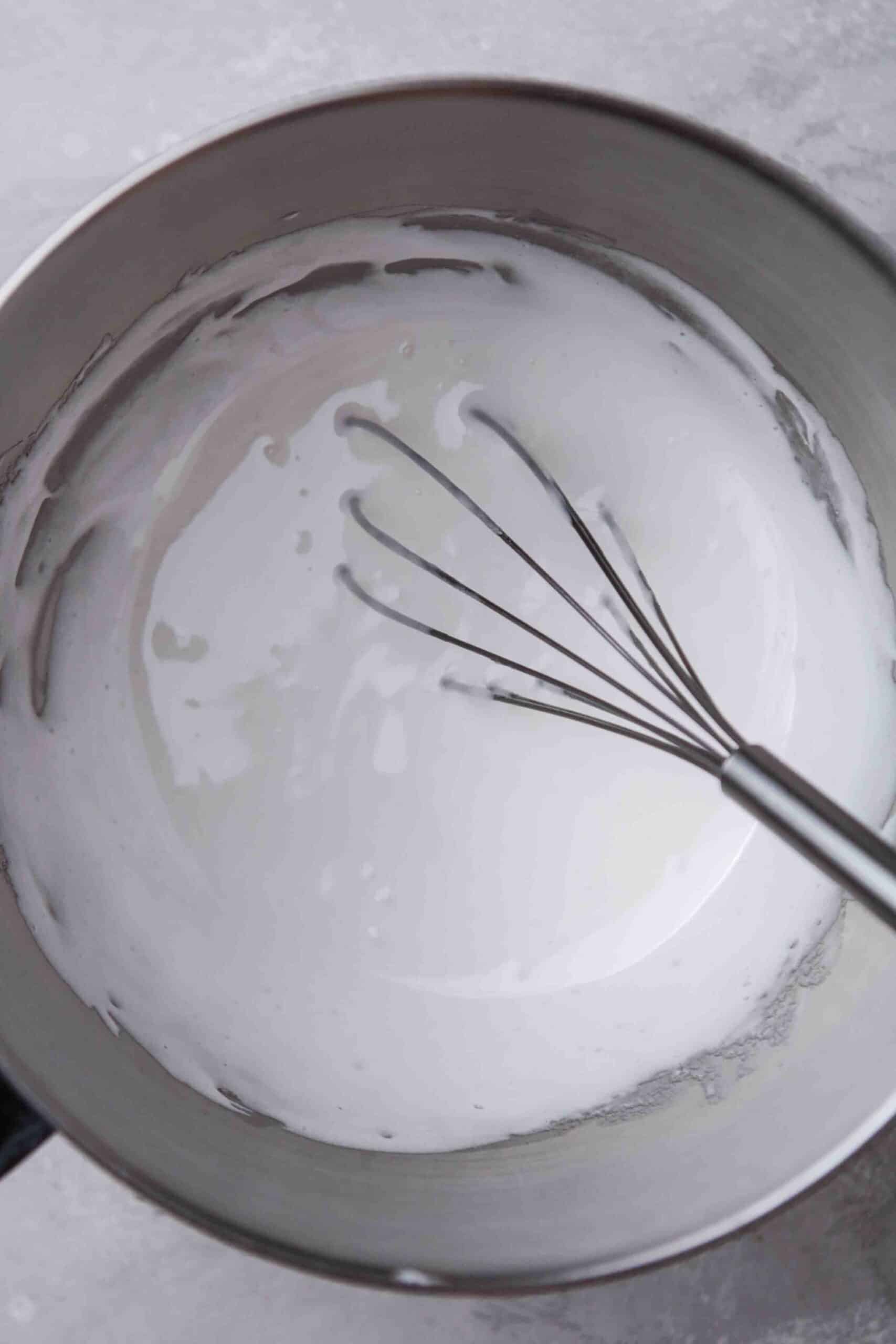 Smooth white buttercream in a stand mixer bowl with the whisk attachment.