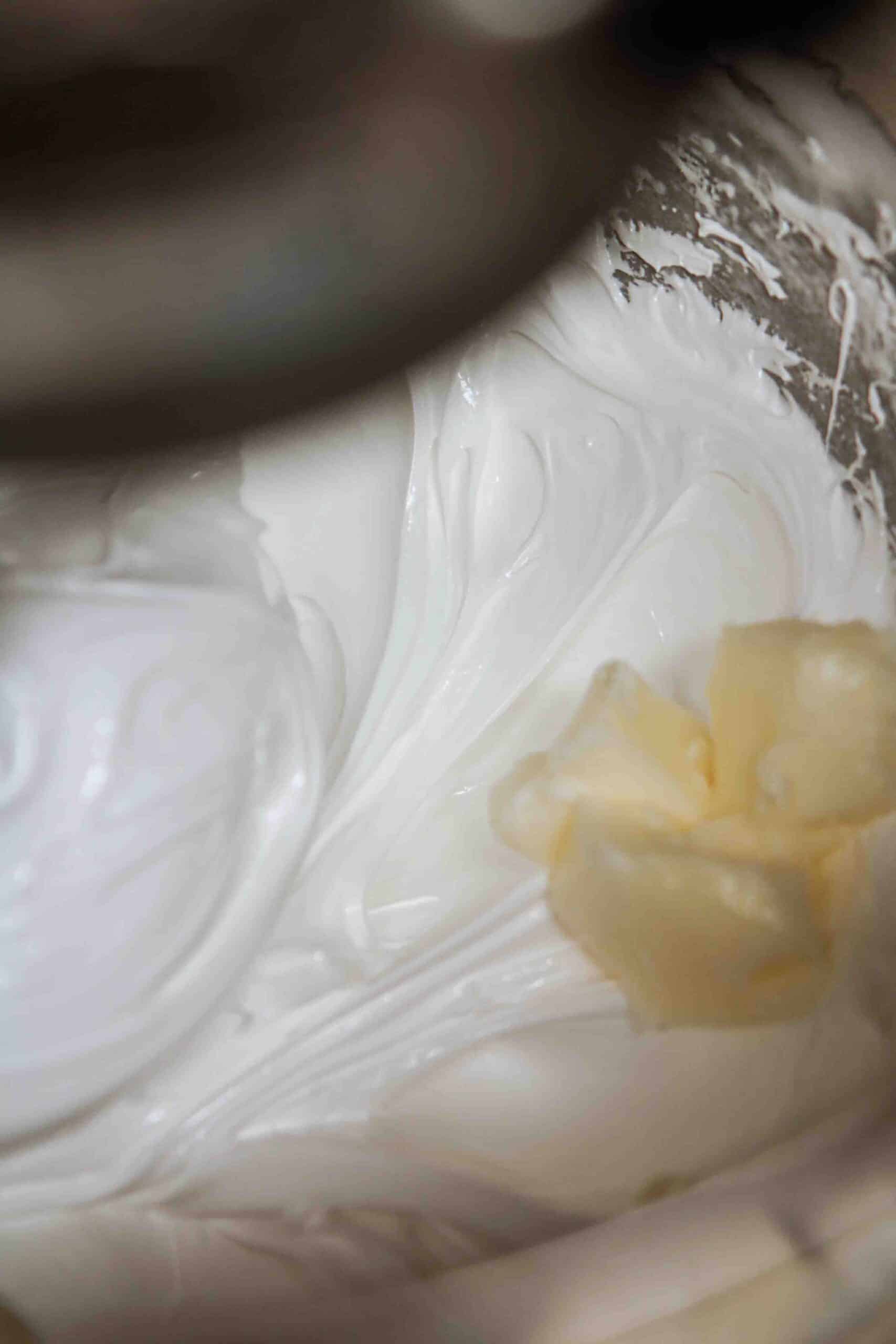 Softened butter added to whipped meringue in a stand mixer bowl.