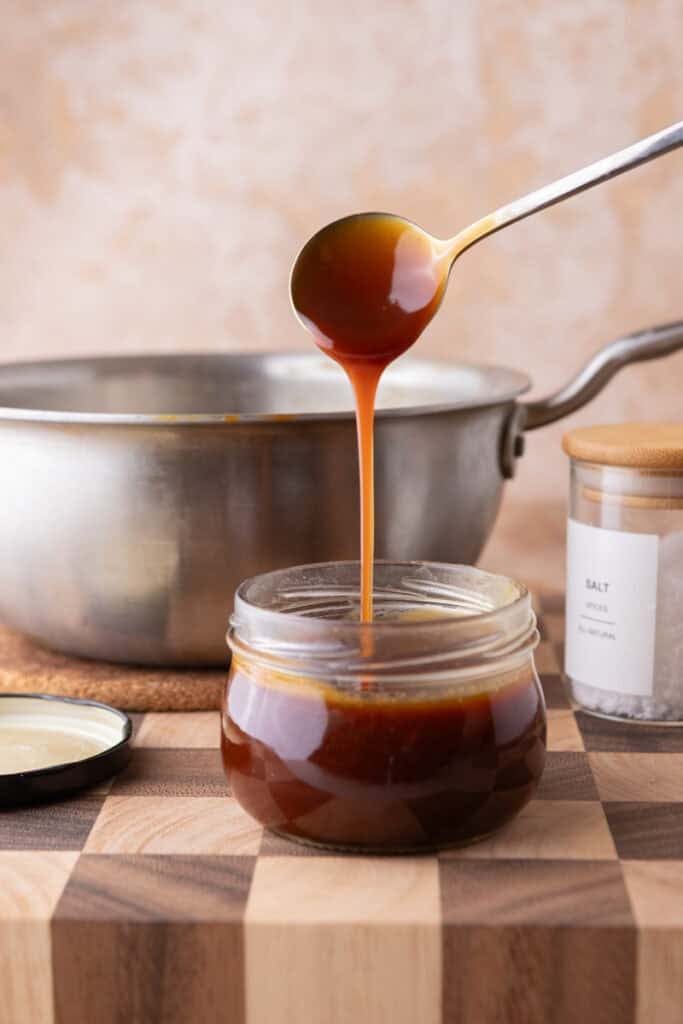 Spoon pouring homemade caramel sauce into jar