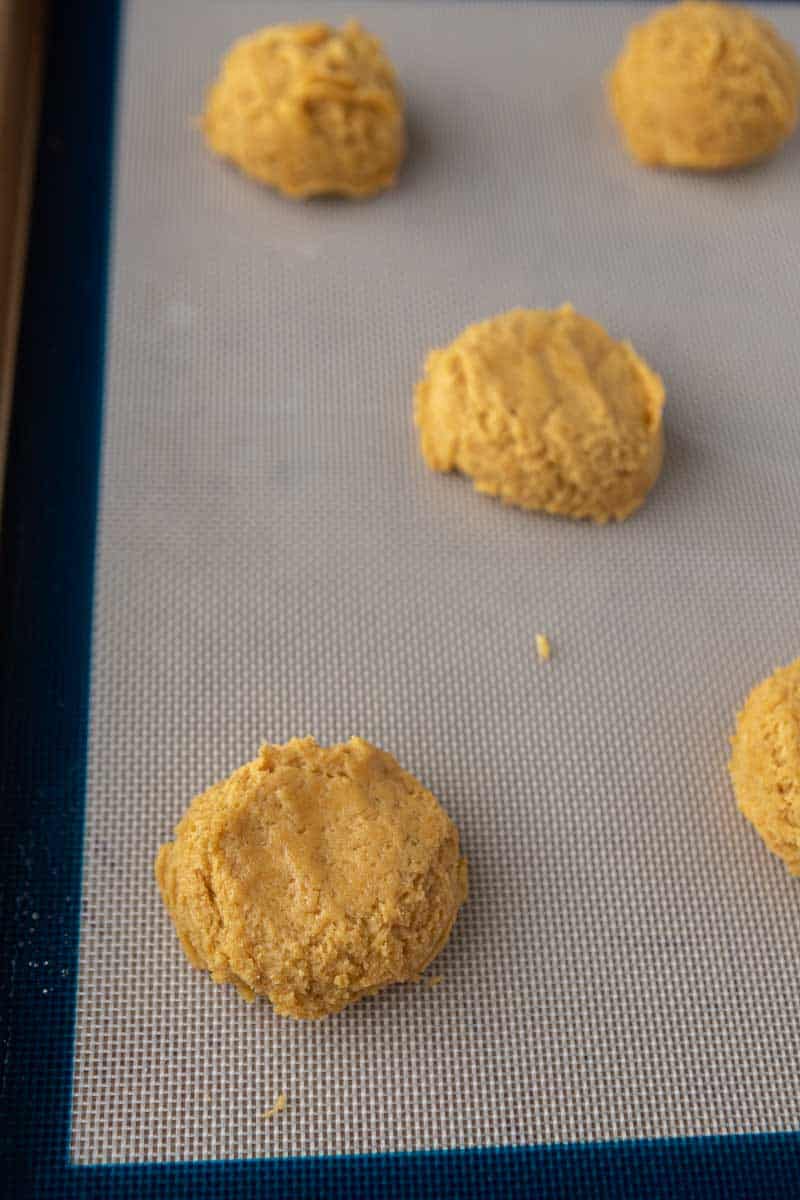 Eight pumpkin cookie dough balls on a parchment-lined baking sheet.