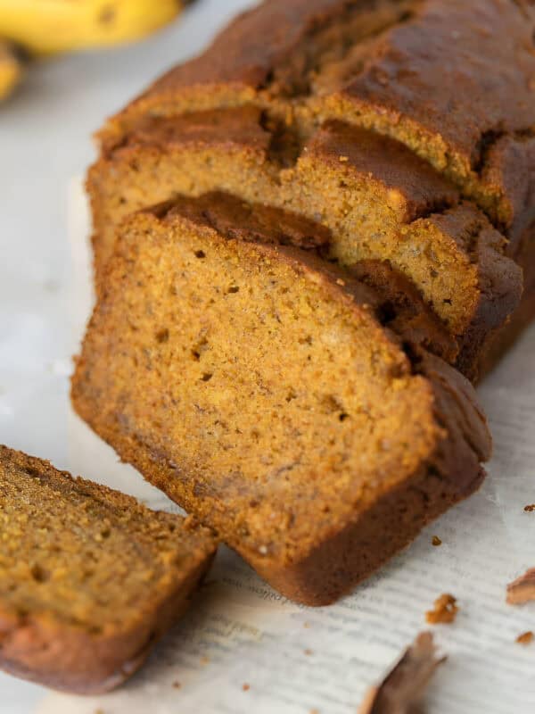 Slices of moist pumpkin banana bread fanned in front of the loaf with cinnamon sticks nearby.