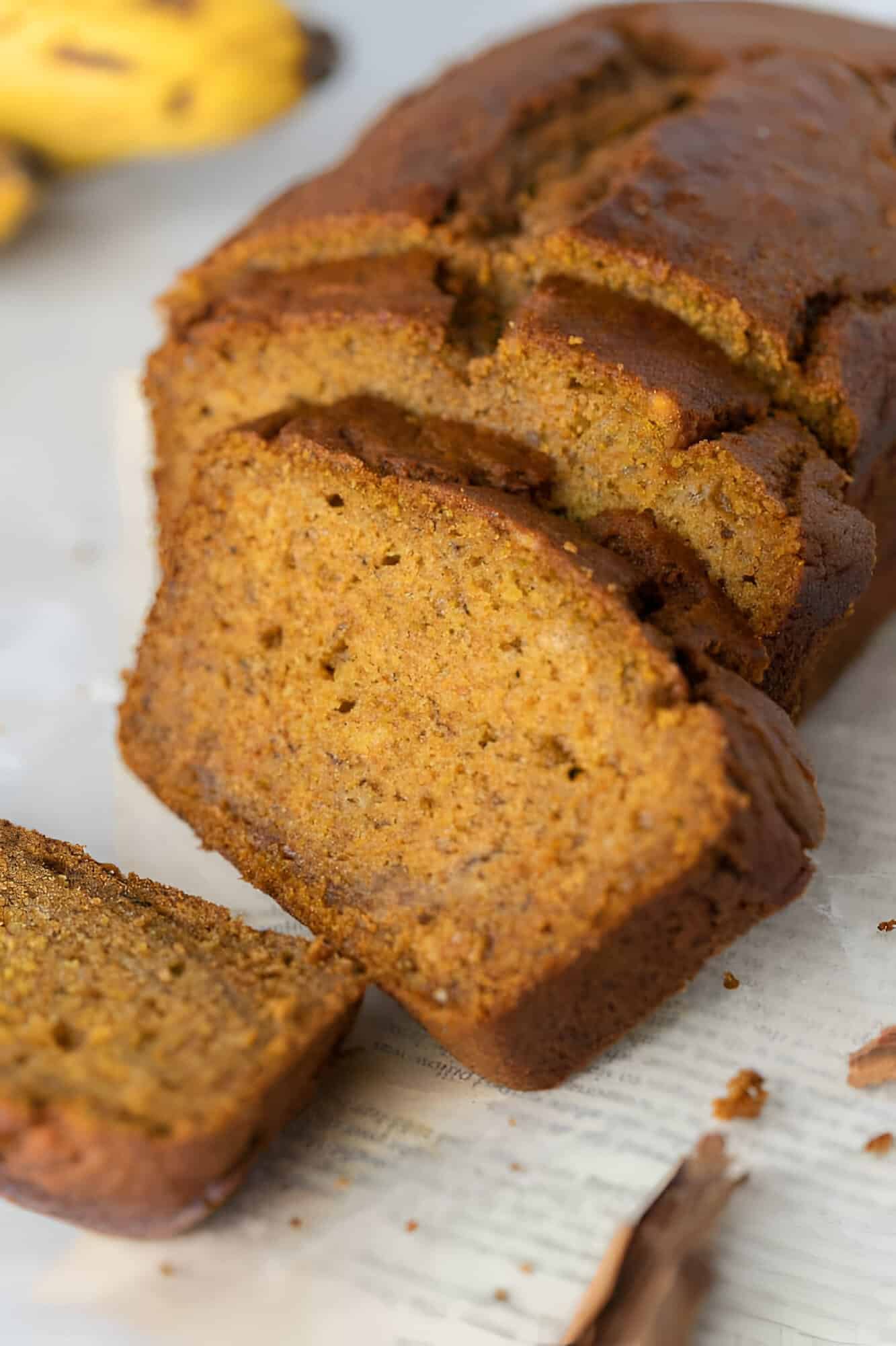 Slices of moist pumpkin banana bread fanned in front of the loaf with cinnamon sticks nearby.