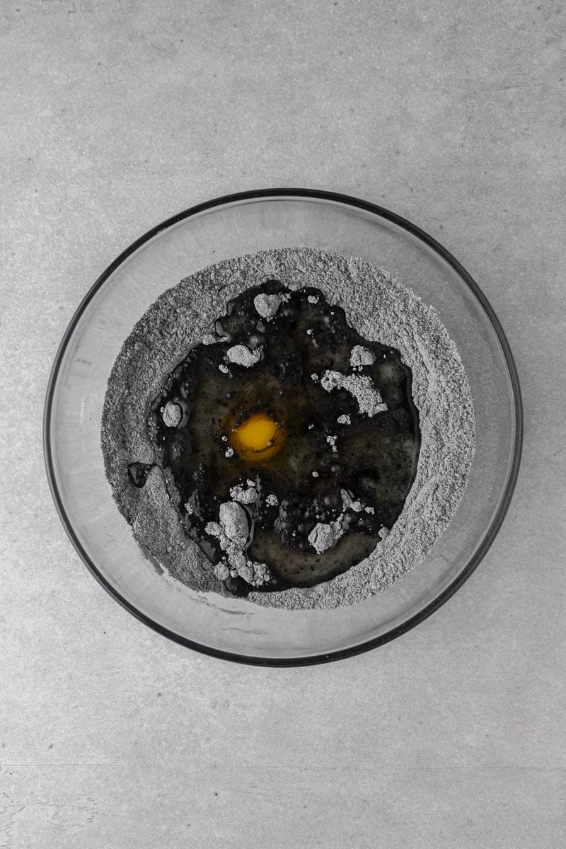 An egg and the wet ingredients added to a well in the black cocoa dry ingredients.