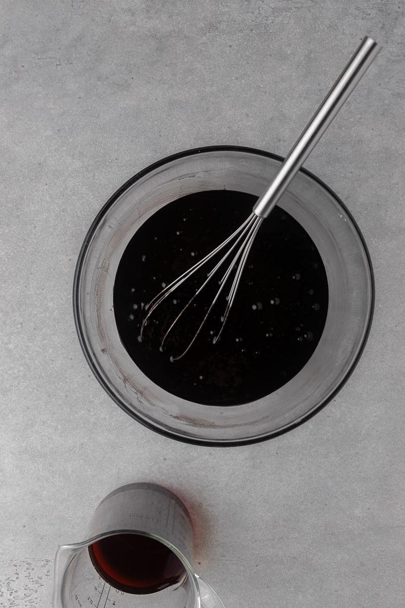 Hot coffee being poured into black velvet cupcake batter in a glass bowl.