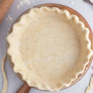 Unbaked pie crust with fluted edges and fork docking in a pie dish, ready for blind baking.