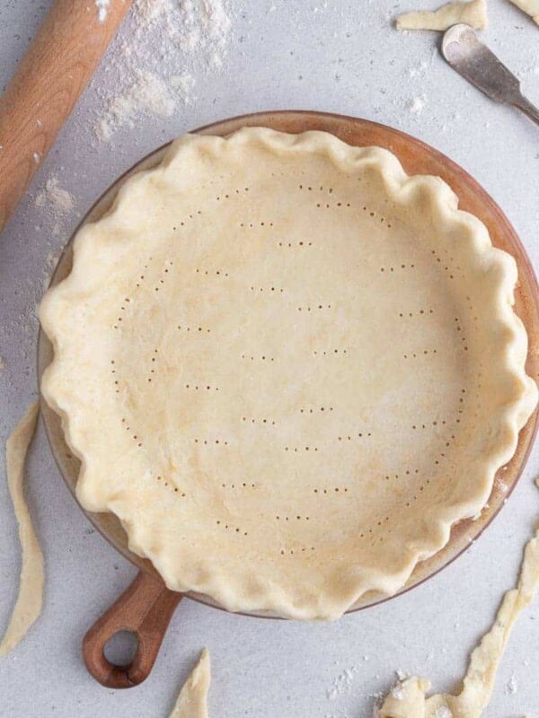 Unbaked pie crust with fluted edges and fork docking in a pie dish, ready for blind baking.