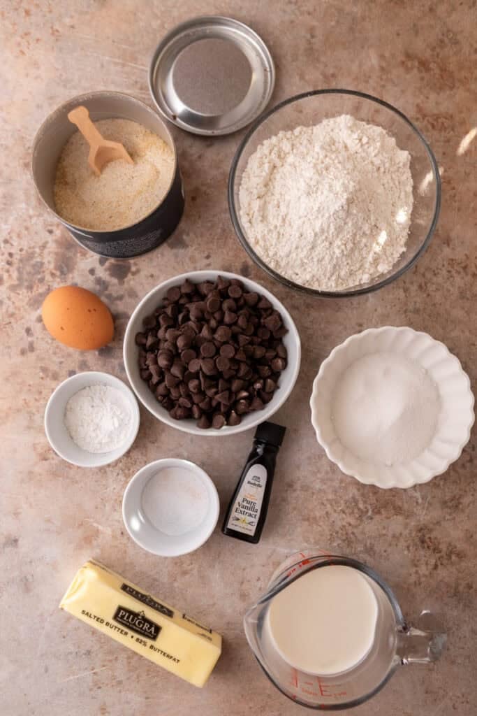 Ingredients for chocolate chip scones displayed on a table, including butter, flour, sugar, eggs, cream, and chocolate