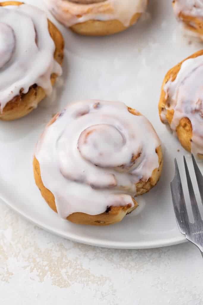 Air fryer cinnamon rolls topped with a gooey glaze on a while plate
