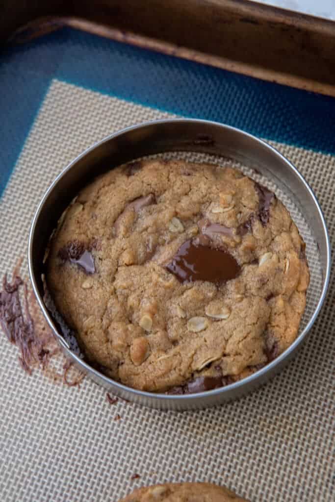 A warm baked cookie being swirled inside a round cookie cutter to give it perfect edges.