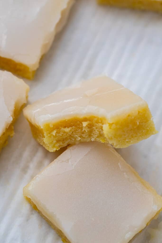 Lemon blondies with a smooth lemon glaze sliced into squares showing the bright yellow fudgy interior with a bite taken out