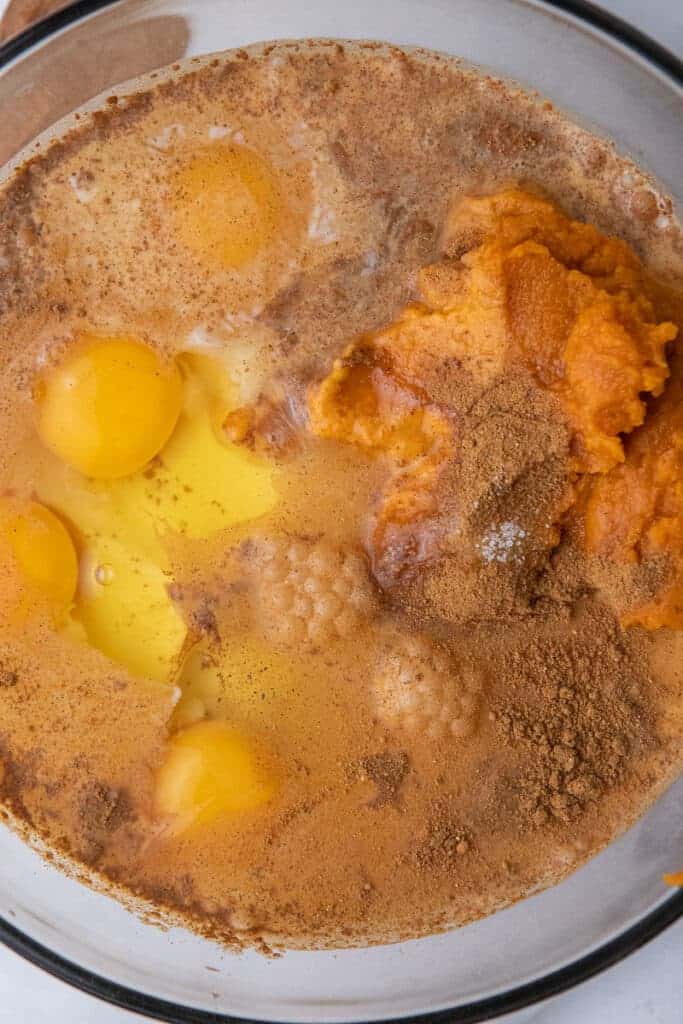 Pumpkin puree, sugar, pumpkin pie spice, salt, eggs and evaporated milk whisked in a glass bowl.