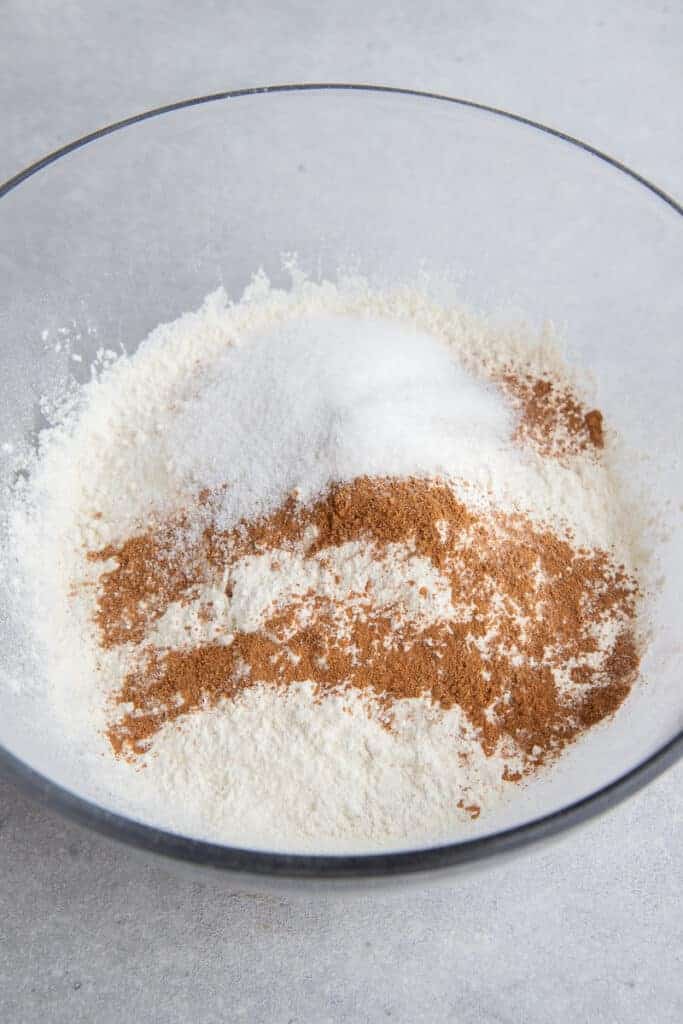 Pancake mix, sugar, and pumpkin pie spice whisked together in a large white mixing bowl.