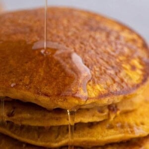 Four pumpkin pancakes cooking on a buttered nonstick pan with bubbles forming across the surface.