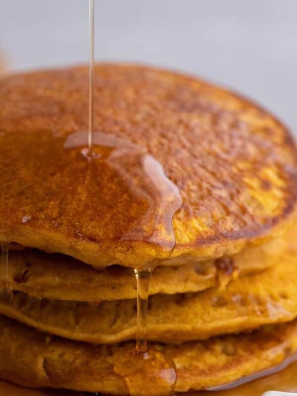 Four pumpkin pancakes cooking on a buttered nonstick pan with bubbles forming across the surface.