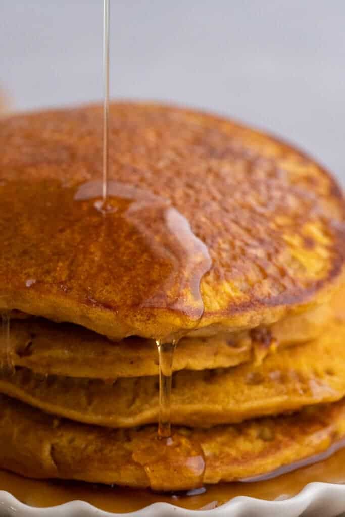 Four pumpkin pancakes cooking on a buttered nonstick pan with bubbles forming across the surface.